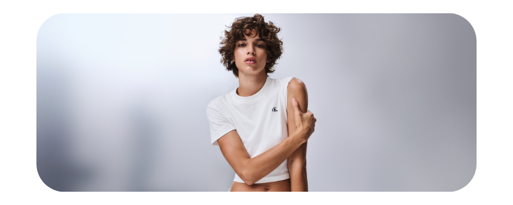 Woman with curly hair wearing a white Calvin Klein cropped t-shirt.