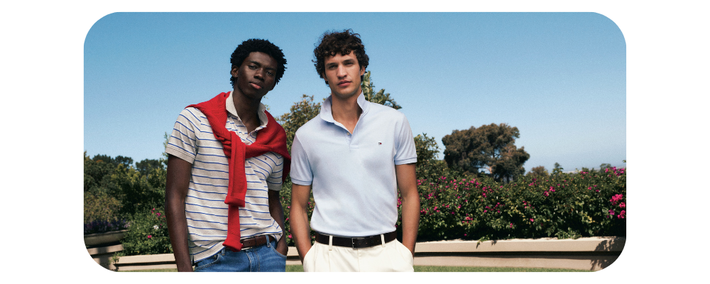 Two men wearing luxury polo shirts and trousers standing outdoors in a garden.