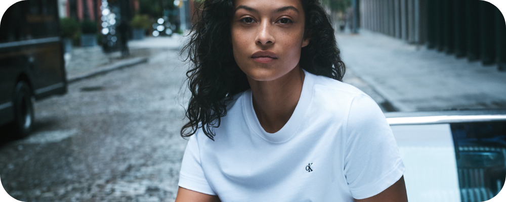 Woman wearing a white Calvin Klein t-shirt standing on a city street.