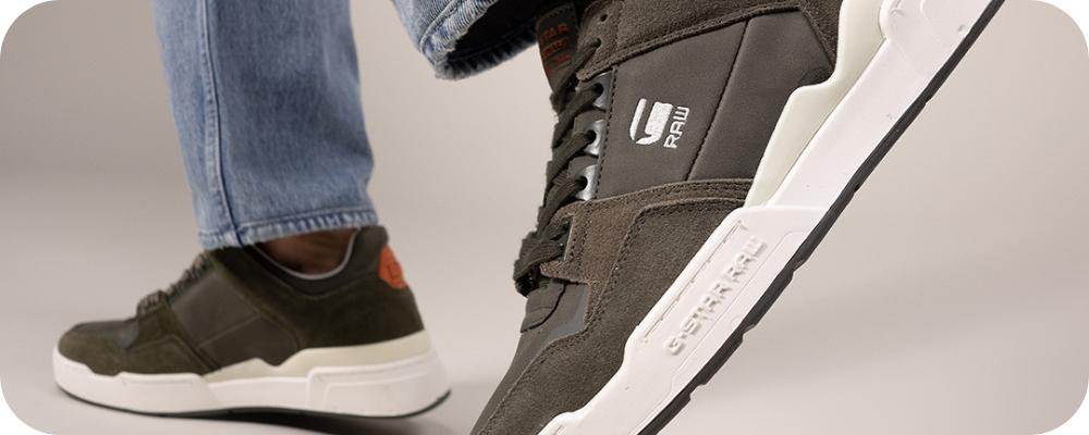 Close-up of olive green G-Star Raw sneakers worn with light blue denim jeans.