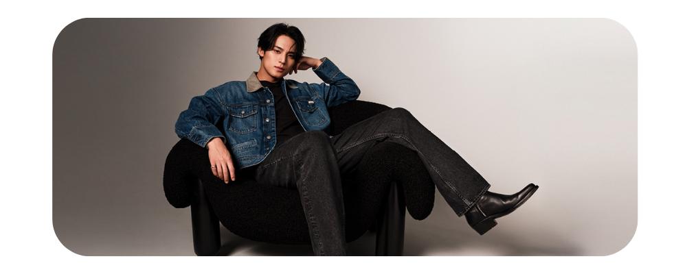 Man wearing a blue denim jacket and black jeans lounging in a black textured chair.