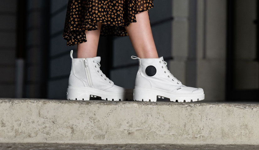 Woman wearing white Palladium chunky ankle boots with side zippers on concrete steps.